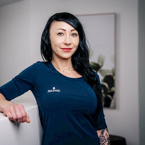 Porträt von Natascha Mörschel, Mitarbeiterin in der Zahnarztpraxis steht lächelnd in blauem Shirt vor Praxisempfang.